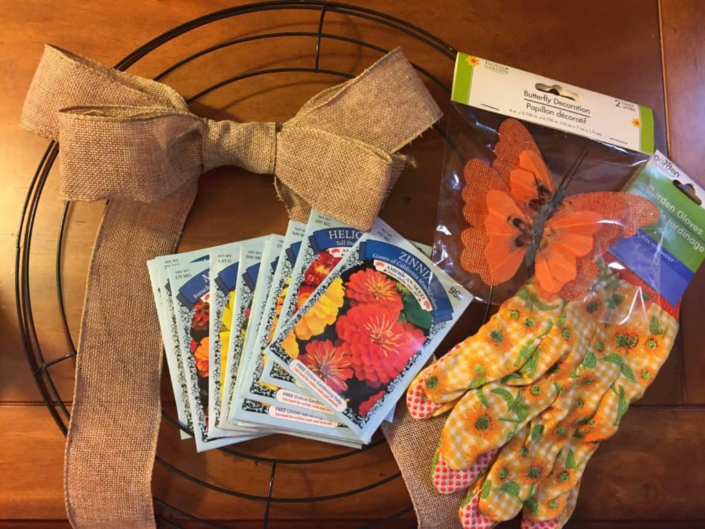 The materials you need to make a spring wreath include flower seed packets, burlap ribbon, a butterfly decoration, a pair of gardening gloves and a wire wreath frame.